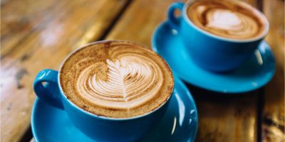Two blue cups of coffee with latte art on wooden table.