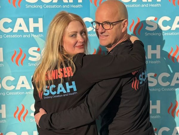 Heidi and Martin hugging in front of a Smoking Cessation and Health banner.