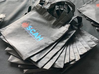 Stack of black tote bags with SCAH logo on a black surface.