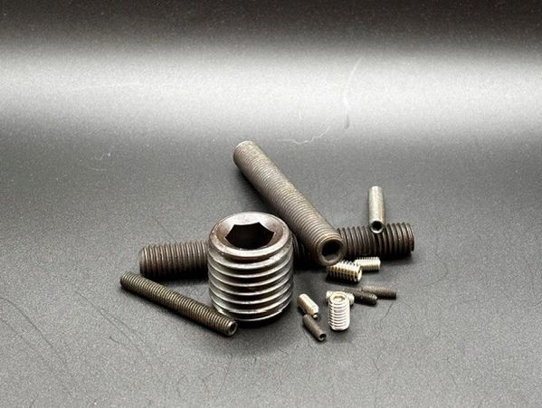 Various sizes of metal threaded inserts on a dark surface.