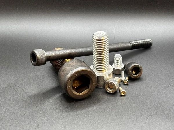Various sizes of metal bolts and screws on a dark surface.