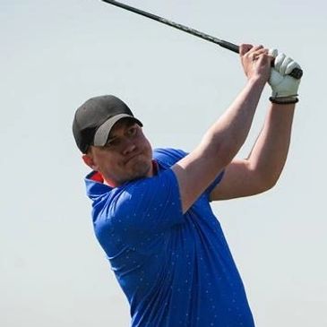 Man in blue shirt swinging a golf club on a clear day.