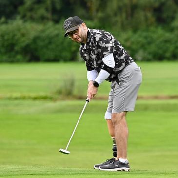 Man with prosthetic leg playing golf on a green course.