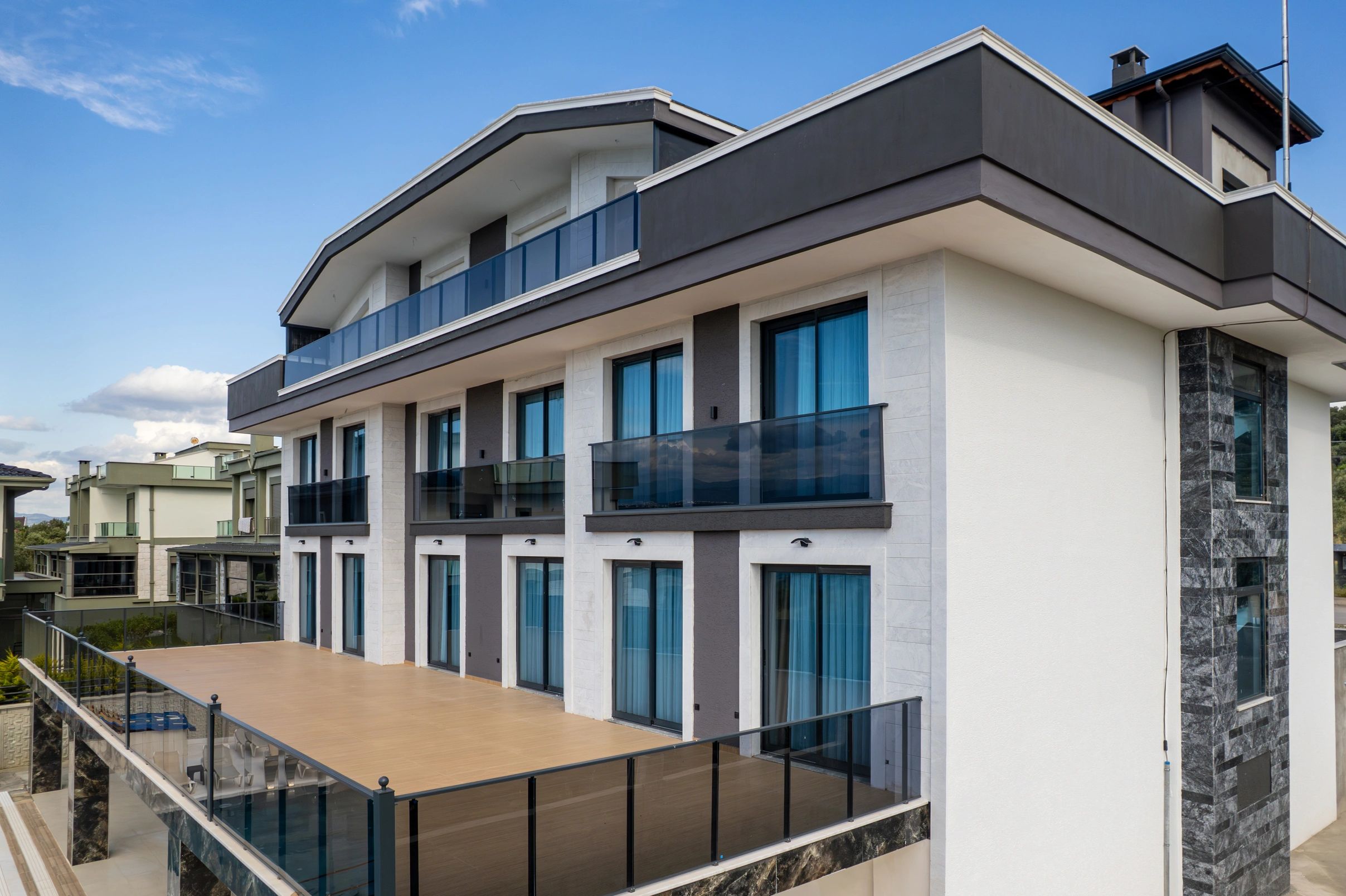 Modern multi-story building with glass balconies and large windows under a clear blue sky.