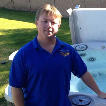 Man in a blue shirt stands beside a filled hot tub in a backyard.