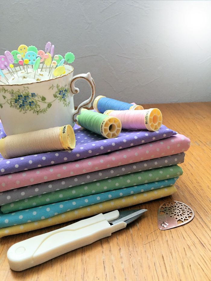 Sewing essentials with colorful fabrics, threads, and pins in a teacup.