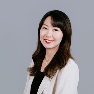 Professional portrait of a smiling woman with long dark hair in a white blazer.