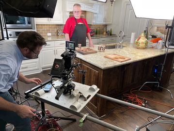 Cinematographer, Shane George, filming a chef preparing meat in a kitchen studio setup.