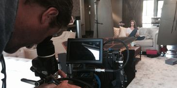 Filmmaker, Shane George, adjusting camera while an actress sits on a sofa in a cozy room.
