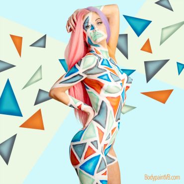 Woman with colorful geometric body paint and pink hair posing.