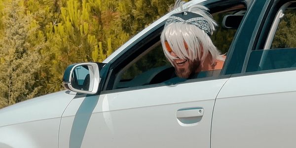 Man with white hair and bandana smiling in a white car.