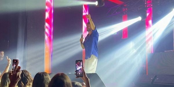 A performer on stage engages the crowd with bright lights and raised fist.