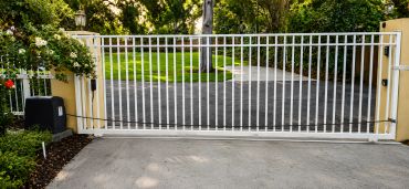 White metal gate across a driveway with greenery around.
