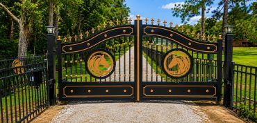 Decorative black and gold iron gates at the entrance of a driveway.