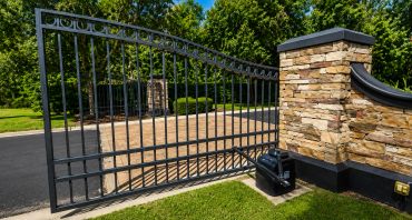Modern automatic driveway gate opening beside stone pillar.