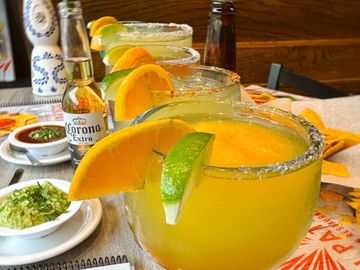 Mango margaritas garnished with lime and orange slices, alongside Corona beers and dipping sauces.