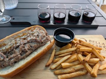 Pulled pork sandwich with fries and a flight of red wines on a wooden board.