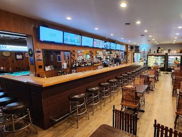 Cozy bar with wooden stools and multiple TVs above the counter.