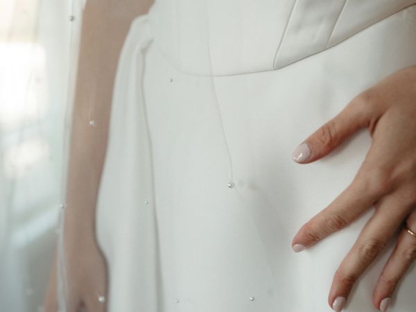 Close-up of a bride's hand resting on a white wedding dress with delicate beading.