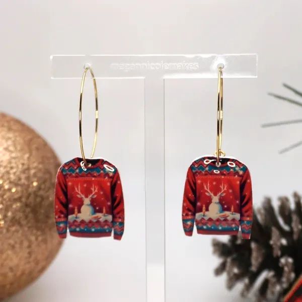 Festive earrings shaped like holiday sweaters with a reindeer design.