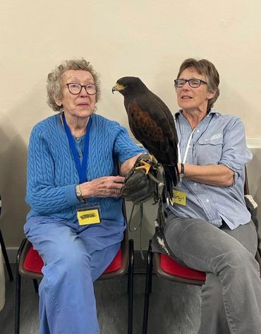 Two women seated with a large bird perched on a gloved hand.