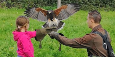 A young girl and man hold a hawk with wings spread outdoors.