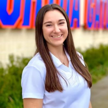 Young woman smiling outdoors in front of a colorful sign.