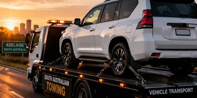 A white SUV is being towed on a flatbed truck during sunset.