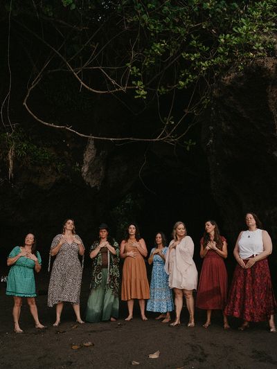 A group of women standing barefoot in a line with hands on their chests outdoors.