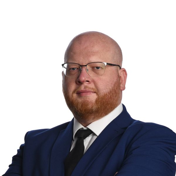 Confident bald man with glasses in a blue suit and black tie.