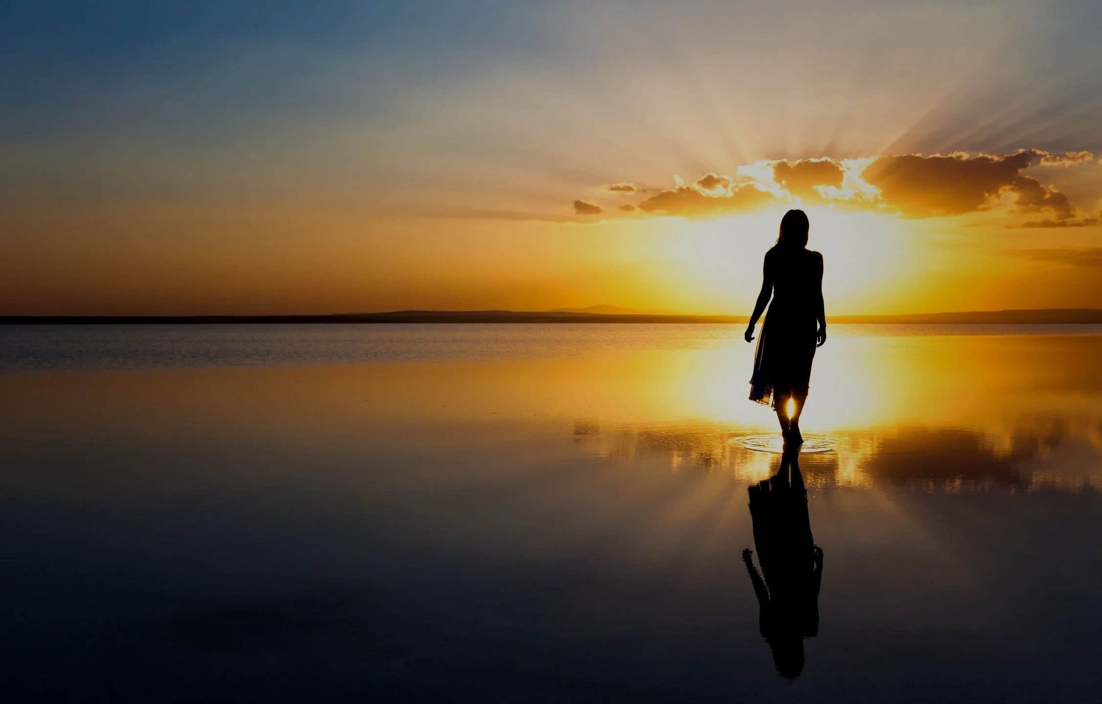 Silhouette of a woman walking on water during a golden sunset.