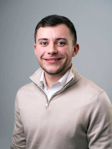 Smiling young man in a beige zip-up sweater.