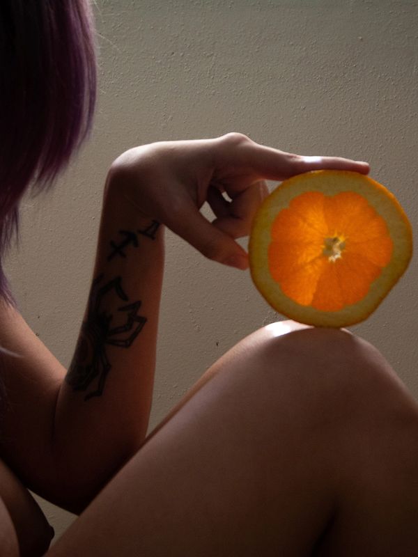 Person holding a glowing orange slice with tattoos on arm.