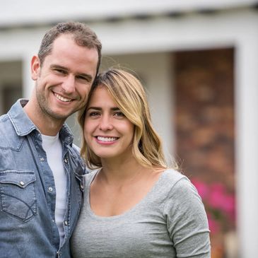 Smiling couple posing happily in front of a house.