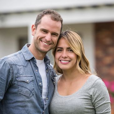 Smiling couple posing happily in front of a house.