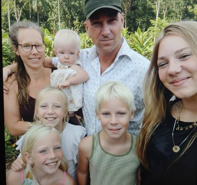 A cheerful family photo with parents and five children outdoors.