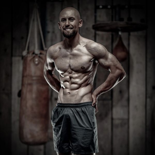 Muscular man posing in a boxing gym with punching bags in the background.