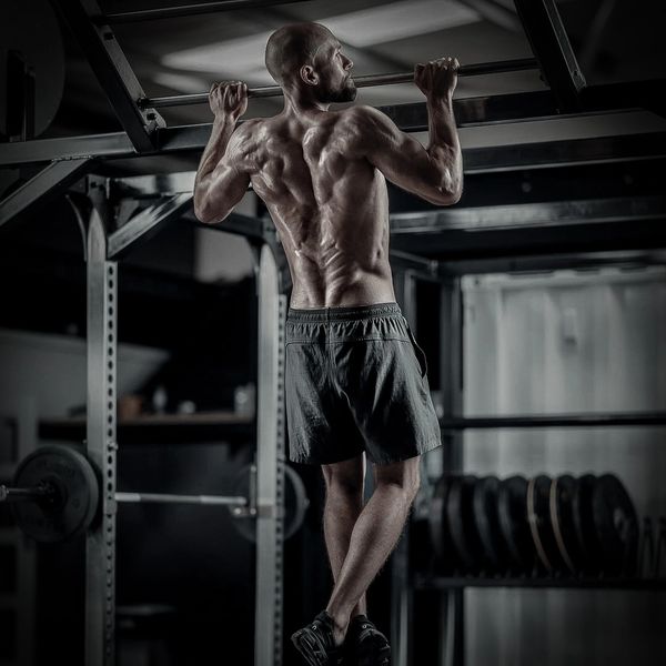 Muscular man doing pull-ups in a gym, showcasing his defined back muscles.