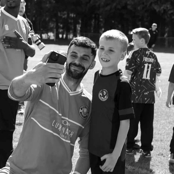 A man and a boy in sports jerseys take a selfie together on a sunny day.
