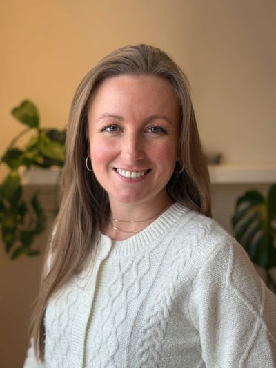 Smiling woman in white sweater with plants in the background.