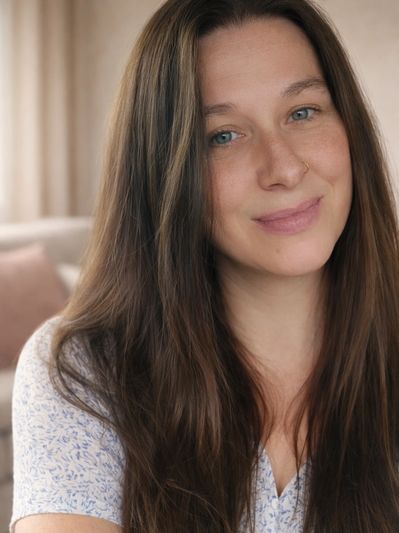 Smiling woman with long brown hair and blue eyes in a cozy indoor setting.