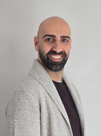 Smiling bald man with a beard wearing a gray knitted sweater.