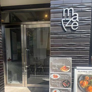 Entrance of a cafe named 'Maze' with menu boards displaying seasonal fruit dishes.