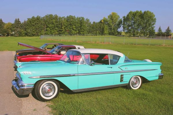 Two vintage cars parked on grass, one turquoise and white, the other red with its hood open.