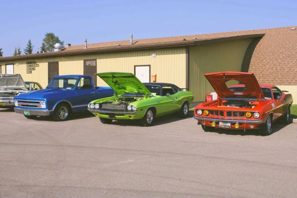 Classic cars and a blue pickup truck parked outside a community curling club.