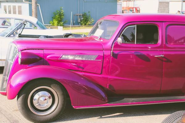 A shiny magenta vintage car parked outdoors on a sunny day.