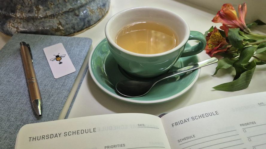 A cup of tea, a pen on a notebook, and an open planner with Thursday and Friday schedules.