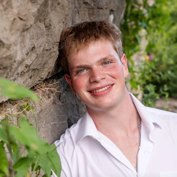 Young man smiling outdoors by a rock wall.