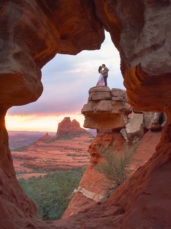 Couple kissing on a rock formation at sunset in a desert landscape.