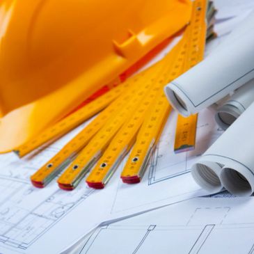 Construction helmet, measuring tools, and blueprints on a table.